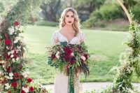 a round wedding arch covered with greenery, white and burgundy blooms and a matching wedding bouquet