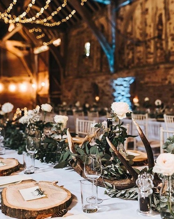 a rustic winter wedding table with wood slice placemats, antlers, greenery and white roses for a chic look
