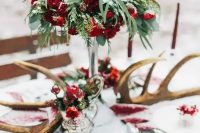 a rustic winter wedding tablescape with greenery and red and burgundy blooms, antlers, red linens for a woodland feel