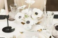 a stylish modern winter wedding tablescape with a white anemone centerpiece, neutral porcelain and a floral menu, black candleholders and cutlery