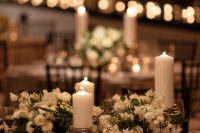 a stylish white winter wedding centerpiece with blooms and pillar candles plus smaller candles around will make your table cozy