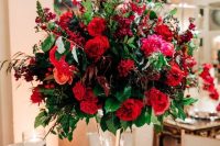 a super bright holiday wedding centerpiece with red and fuchsia blooms, foliage and berries