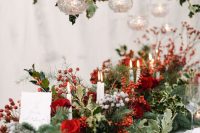 a super lush winter wedding table runner with berries, red roses, candles, greenery and evergreens is a gorgeous idea