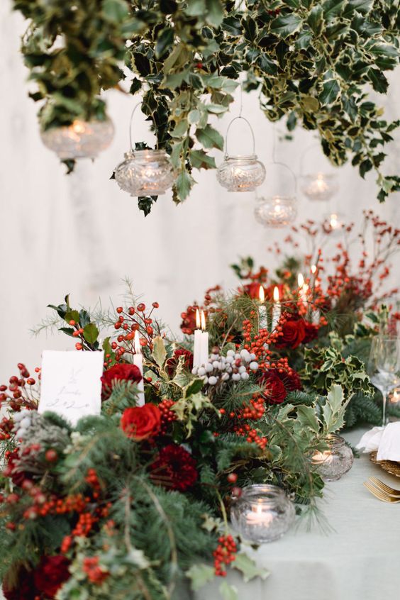 a super lush winter wedding table runner with berries, red roses, candles, greenery and evergreens is a gorgeous idea