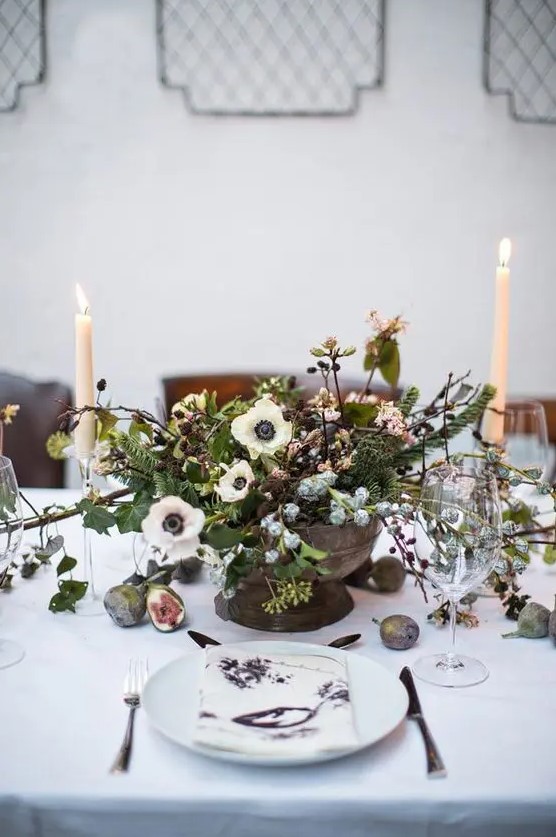 a vintage-inspired centerpiece with white blooms, pinecones, blush flowers, greenery and leaves, all in pale winter shades