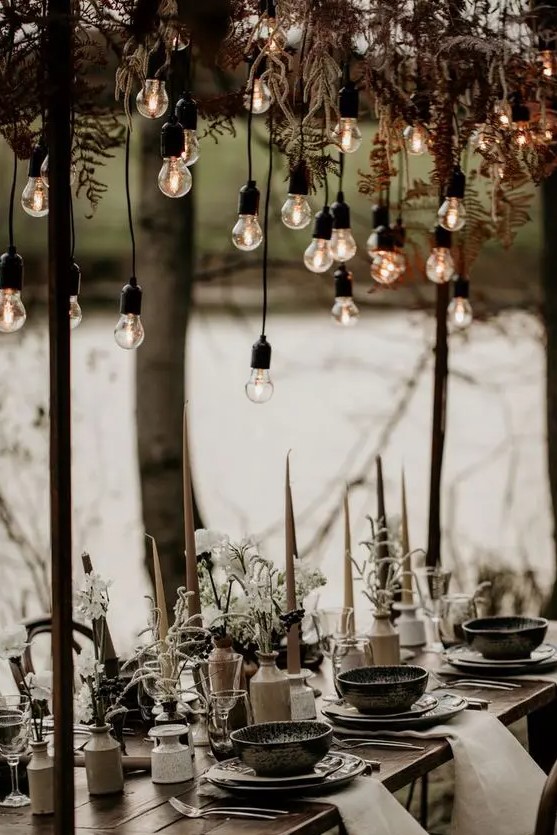 a winter boho wedding tablescape with candles, white blooms and greenery, hanging ferns and bulbs, printed porcelain