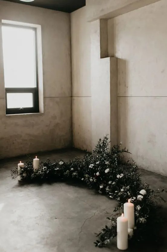 a winter wedding altar of greenery and white blooms and pillar candles is a stylish and cool idea for a minimalist wedding