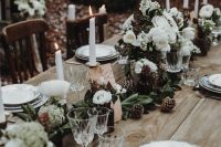 neutral winter wedding centerpieces with bloosm, greenery, pinecones on the table and tall and thin candles