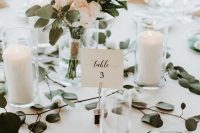 pillar candles in glasses, a blush and greenery wedding centerpiece in a vase make up a modern wedding tablescape