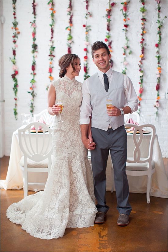 a romantic lace mermaid wedding dress with a high neckline and a train, the groom wearign grey pants, a waistcoat and a tie