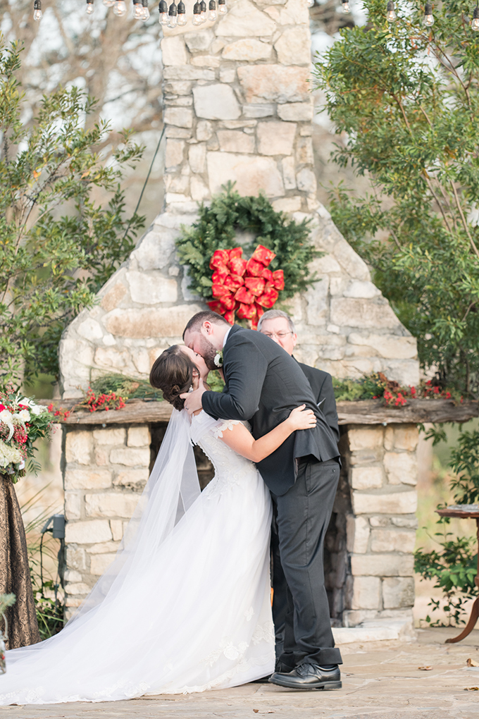 The wedding ceremony took place outdoors, in front of a fireplace decorated with greenery, berries and blooms