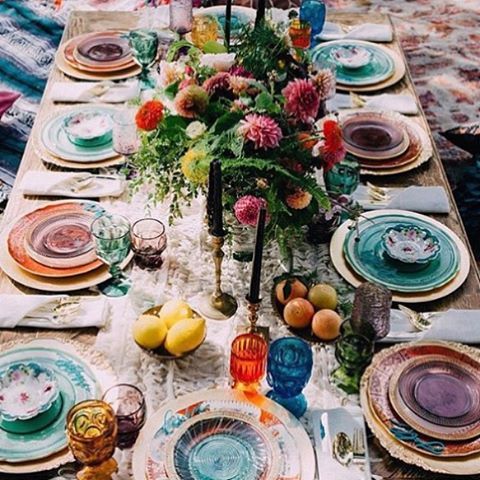 a bright Mediterranean table setting with colored glasses and plates and chargers plus lush florals