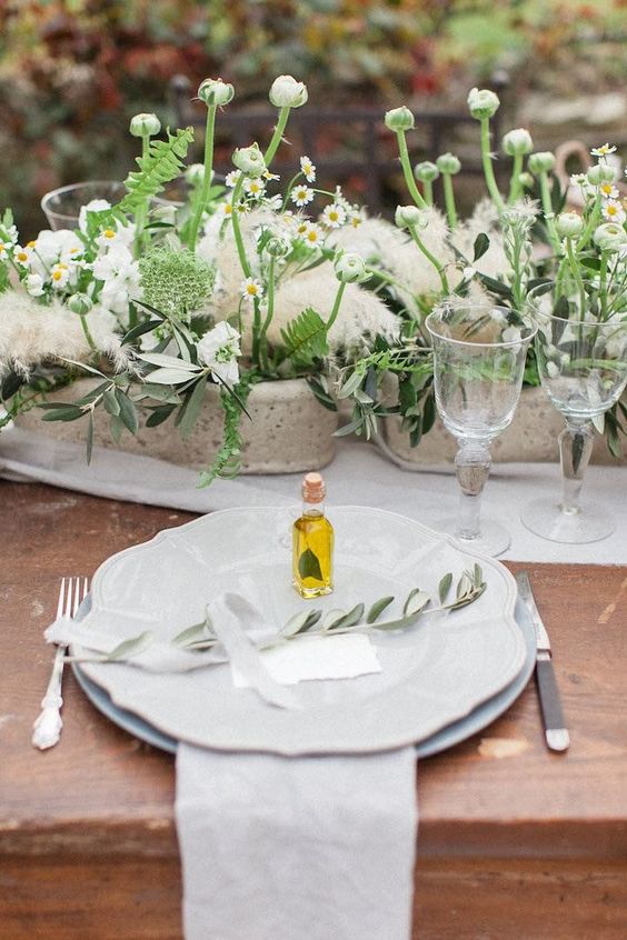 a cozy Mediterranean reception table with neutral textiles and porcelain, potted plants and blooms, pampas grass and olive oil