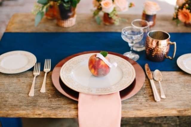 a copper charger, a peachy pink napkin, a real peach as a card holder and a printed peachy plate