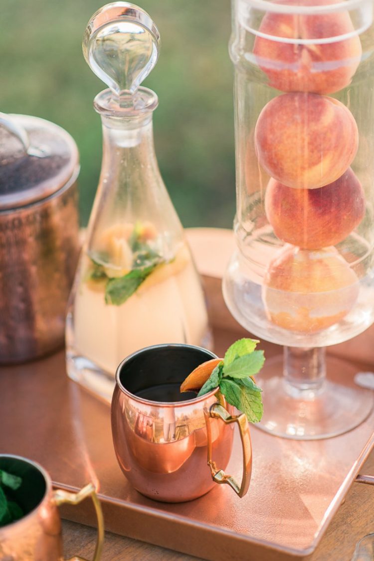 a stylish wedding bar with copper mugs, trays and jars and real peaches in a tall glass vase to add them to drinks
