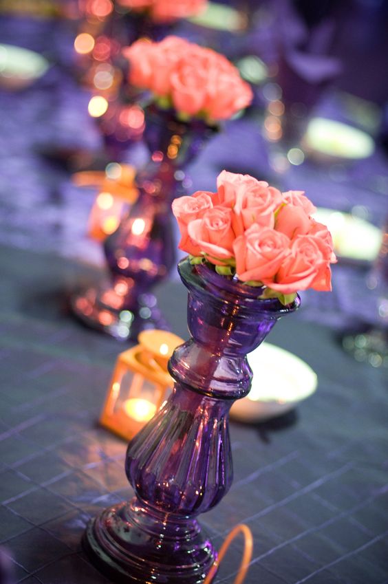 a creative wedding centerpiece of a tall purple vase and some coral roses is a great idea for a boho or Moroccan wedding