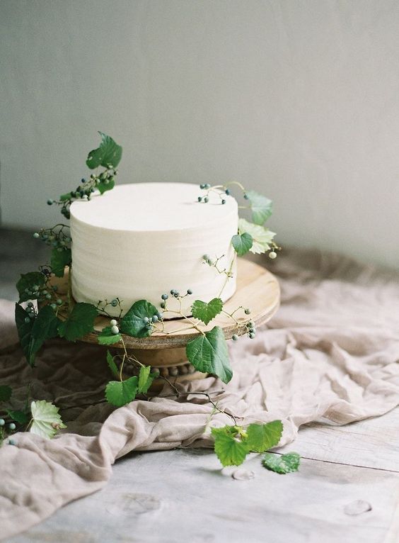 a simple and natural white wedding cake decorated with fresh greenery and berries for a delicate Nordic spring wedding