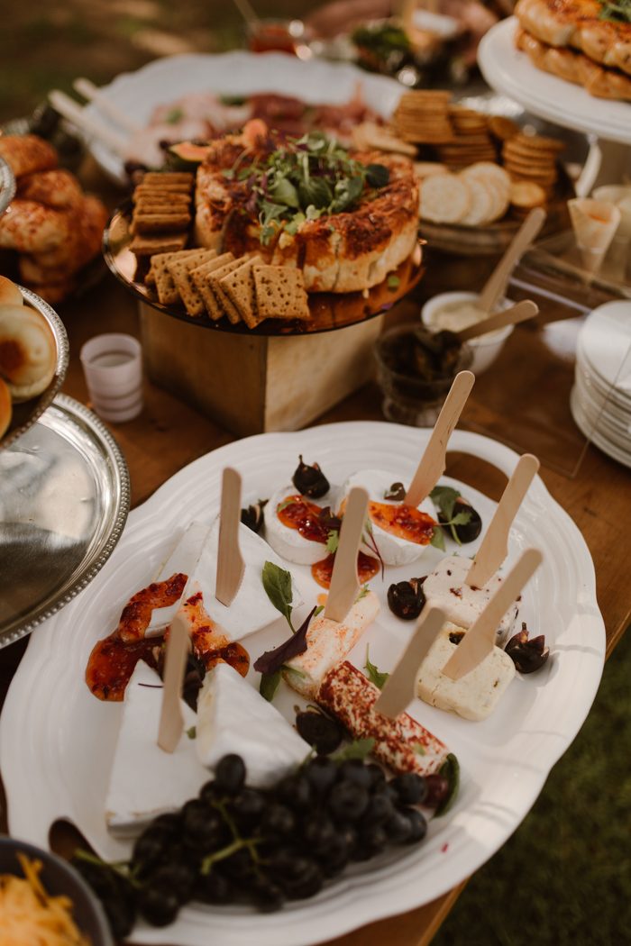 a chic charcuterie board with different types of cheese, grapes, crackers, meat and greenery