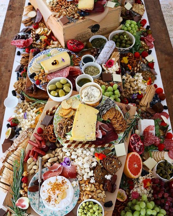 a charcuterie table with lots of types of nuts, vegetables, cheese, salami, crackers and grapes