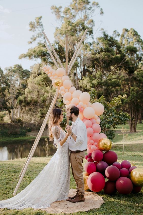 a fresh and modern take on a boho wedding arch with peachy, gold and plum-colored balloons