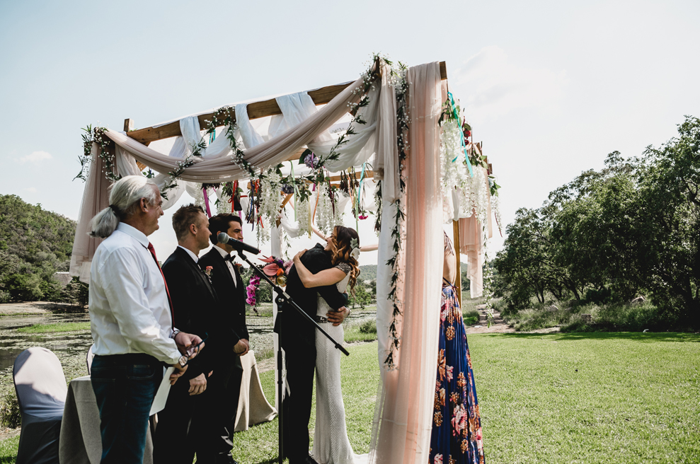 The wedding arch was made of wood, with some blusha nd white fabric and lush blooms hanging down