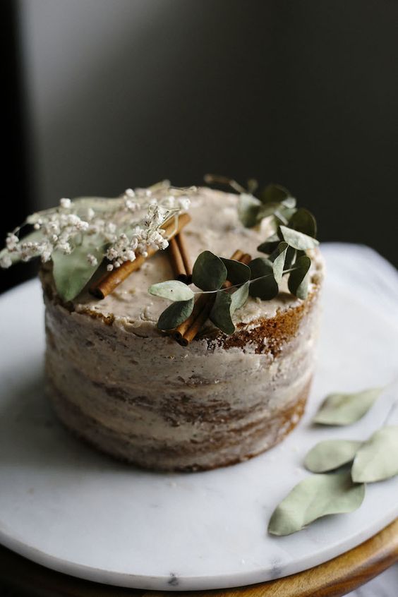 a vegan vanilla cake topped with a smooth chai spice icing and greenery, cinnamon bark and blooms