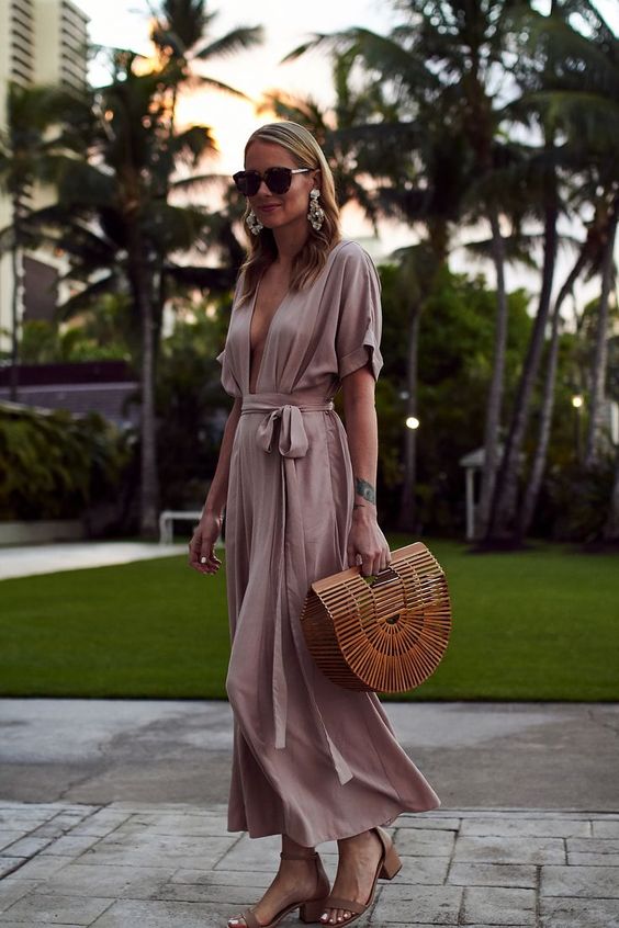 a blush maxi dress with short sleeves, a plunging neckline and a sash, a wooden bag and nude heels