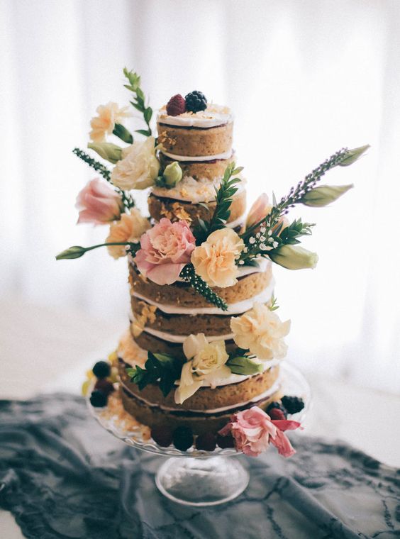 a naked vegan gluten-free wedding cake topped with fresh berries, blooms and some greenery