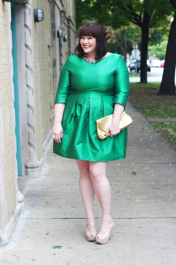an emerald high neckline over the knee dress with long sleeves, nude shoes and a metallic clutch