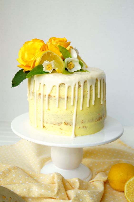 a naked vegan lemon curd layer cake with yellow frosting, dripping and some blooms and citrus on top