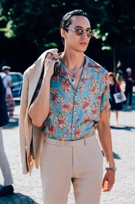 a bold tropical wedding guest look with a blue printed shirt, a tan linen suit and layered necklaces is cool and chic
