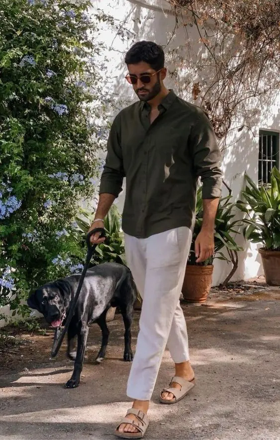 a casual beach wedding guest outfit with a dark green shirt, white linen pants, grey birkenstocks and sunglasses is cool and elegant