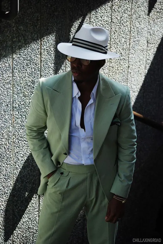 a super elegant beach wedding guest look with a white shirt, a green pantsuit and a hat with a ribbon plus sunglasses
