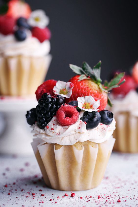 vegan vanilla cupcakes with fresh berries and edible flowers on top are a vegan take on a classic dessert