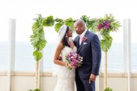 06 a bamboo wedding arch decorated with tropical leaves and hot pink blooms for a tropical wedding