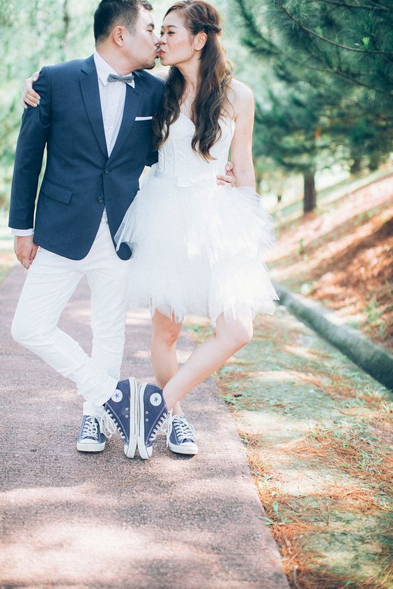 a chic groom's outfit with a navy blazer, white pants, a blue bow tie and blue denim sneakers and the same sneakers for the bride