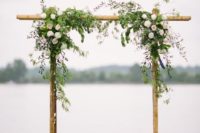 07 a bamboo wedding arch decorated with textural greenery and roses plus petals on the ground looks simple and romantic