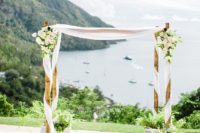 09 a bamboo wedding arch interwoven with white flowy fabric, lush neutral blooms and greenery plus greenery at the base