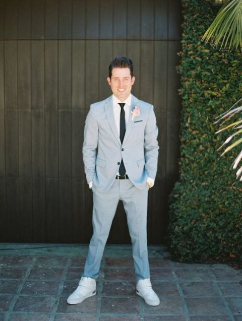 a light blue suit, a white shirt and a black tie plus neutral sneakers and a blush boutonniere is a cool spring outfit