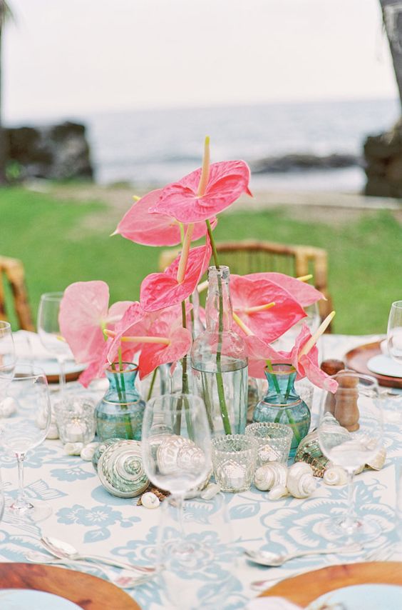 a beachy wedding centerpiece of bright pink anthuriums in blue vases and of seashells