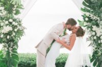 12 a gorgeous tropical wedding arch decorated with white flowy curtains, monstera leaves and white blooms