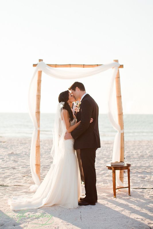 a very simple bamboo wedding arch styled only with some airy white fabric is great for a modern beach wedding