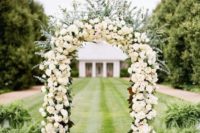 a curved wedding arch decorated with neutral roses and lush greenery plus lots of petals around