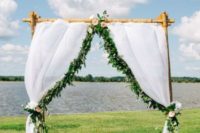 15 a bamboo wedding arch with white curtains, greenery and blush blooms on the lake shore