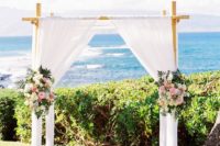 16 a bamboo wedding arch with white flowy and airy curtains, pink and white flowers and greenery