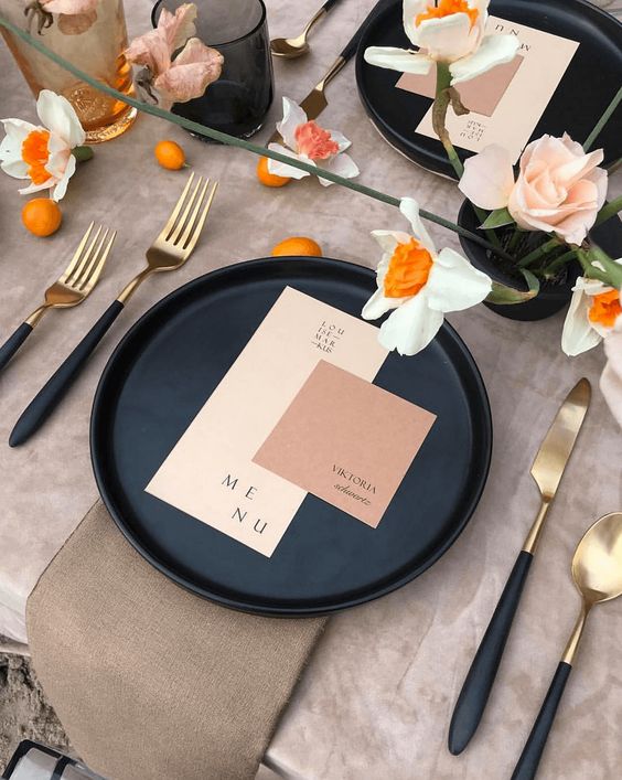 a chic color block wedding setting with blush and dusty pink cards, a black charger and black and gold cutlery