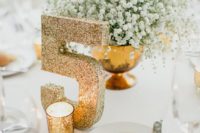 17 a gold bowl with baby’s breath and a gold glitter table number is a chic and elegant setup