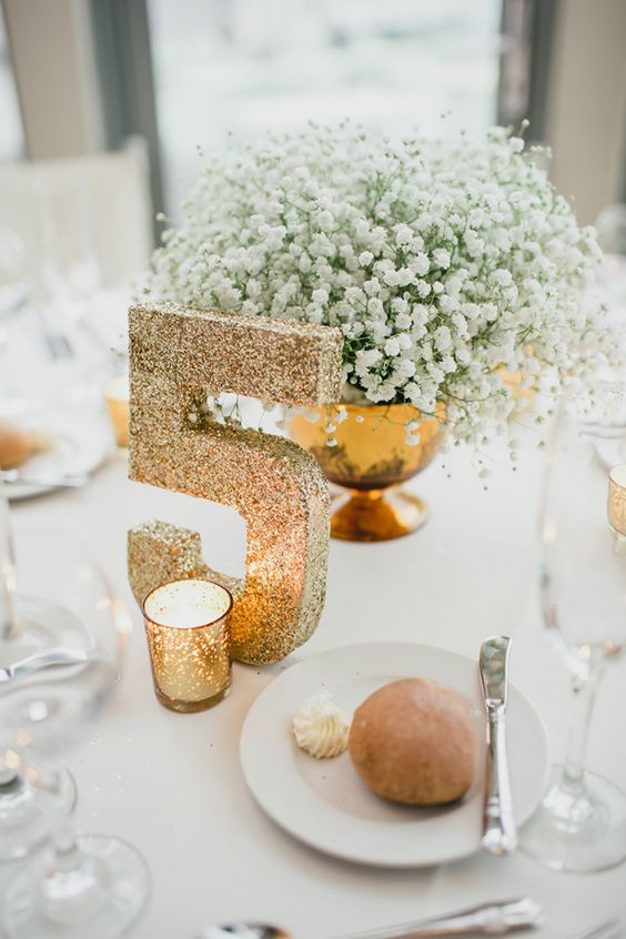 a gold bowl with baby's breath and a gold glitter table number is a chic and elegant setup