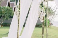 18 a bamboo wedding arbor decorated with white curtains, white and green blooms and greenery