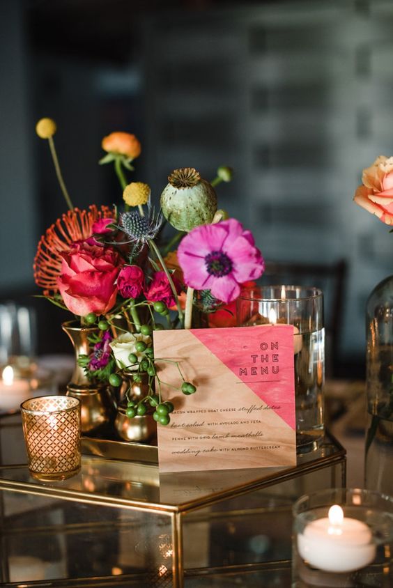 a colorful floral centerpiece and a color block menu plus candles around for color lovers